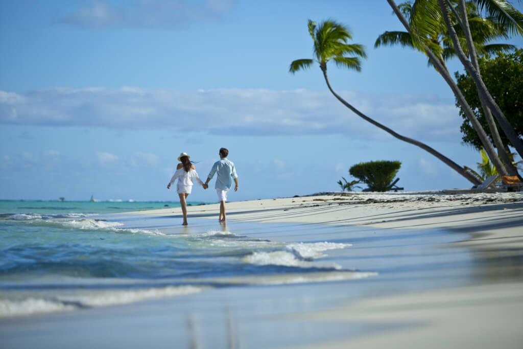 Paar beim Spaziergang am Strand von Bora Bora mit Palmen und Wellen aus der Lagune