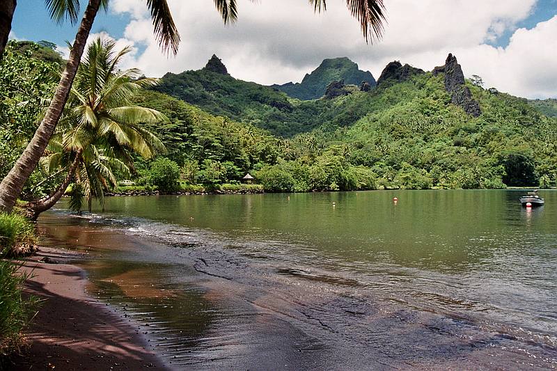 Polynesien Urlaub auf Tahiti mit schwarzem Sandstrand und grün bedeckten Bergen.
