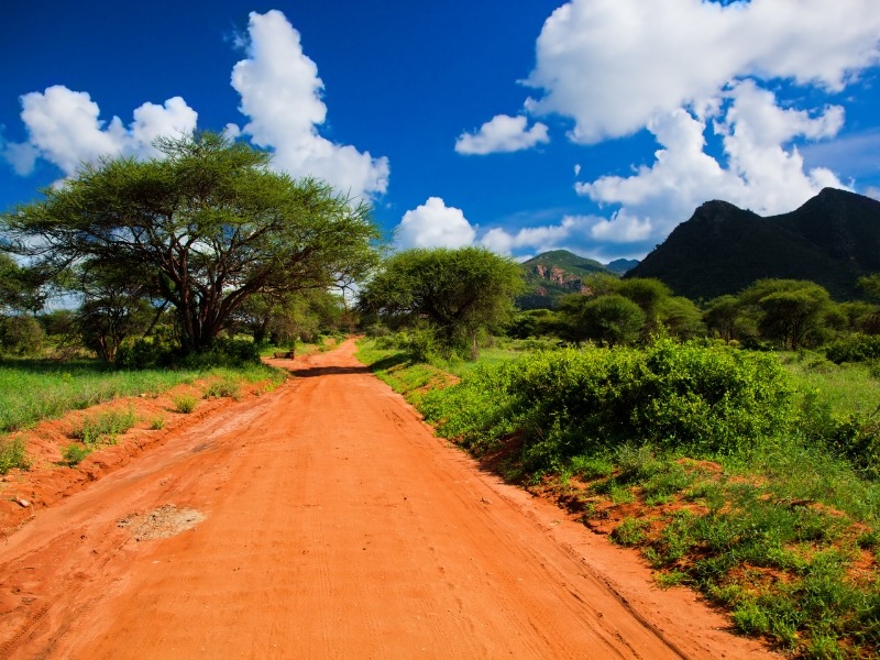 Orange Sandpiste mit Buschland auf Safari im Tsavo Nationalpark in Kenia.