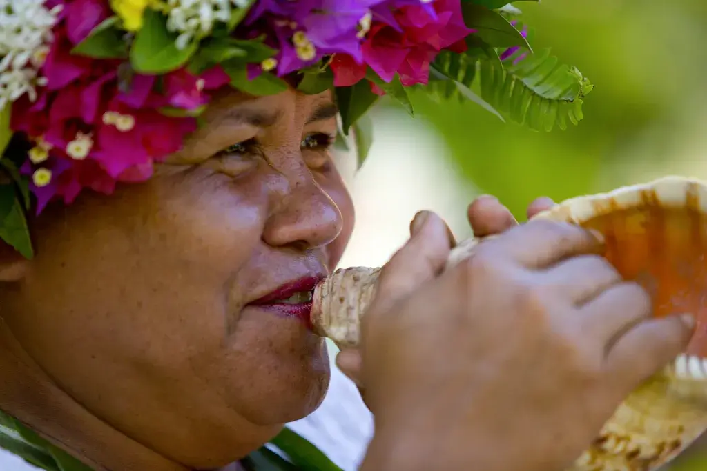 Polynesierin mit buntem Blumenschmuck auf dem Haar bläst in eine Muschel