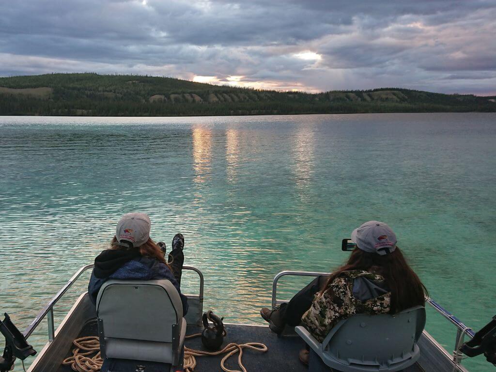 Zwei Frauen im Wildnisurlaub Kanada beobachten den Sonnenuntergang vom Boot aus am See.